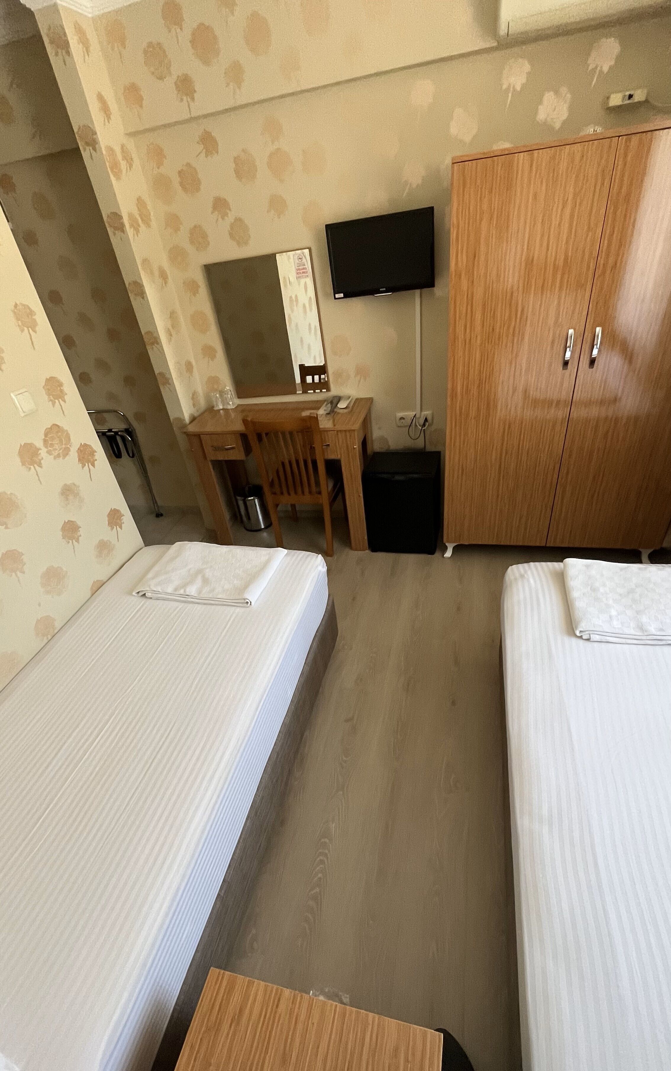 A hotel room with two beds, a desk with a chair, a television, and a wardrobe.