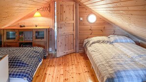 Ein gemütliches Schlafzimmer im Dachgeschoss mit zwei Betten, Holzwänden, einer geneigten Decke und einem kleinen Fenster.