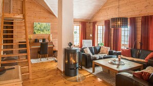 Ein gemütliches Blockhaus-Interieur mit einer Holztreppe, einem Kamin, einem Klavier und bequemen Sitzgelegenheiten.