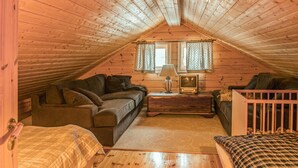 Ein gemütliches Schlafzimmer im Dachgeschoss mit schrägen Holzwänden, einem Sofa, einem kleinen Tisch mit Lampe und einem Babybett.