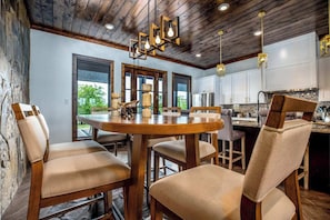 A modern kitchen with a wooden dining table and chairs, a large window, and a stone wall.