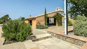 Une maison de style méditerranéen, avec un toit en tuiles, un chemin en pierre et un jardin bien entretenu agrémenté d’arbustes à feuilles persistantes.