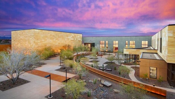 A modern building with a stone facade, a courtyard with plants, and a clear sky.