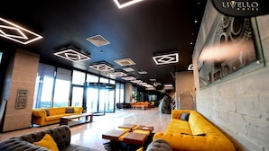 Eine moderne Hotelhalle mit einer zentralen Sitzgruppe, großen Fenstern und geometrischer Deckenbeleuchtung.