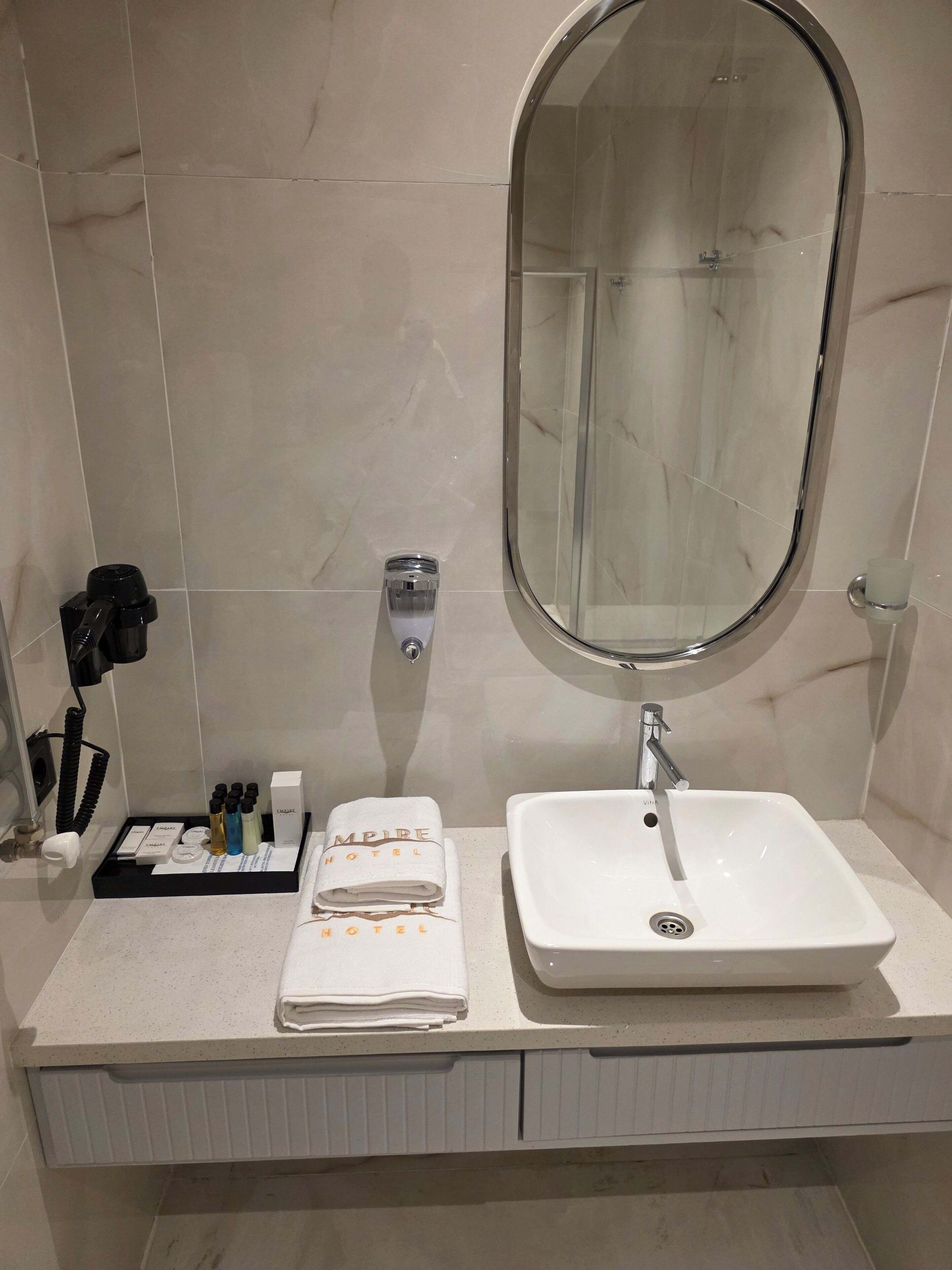 A modern bathroom with a white sink, a large mirror, and a towel rack.