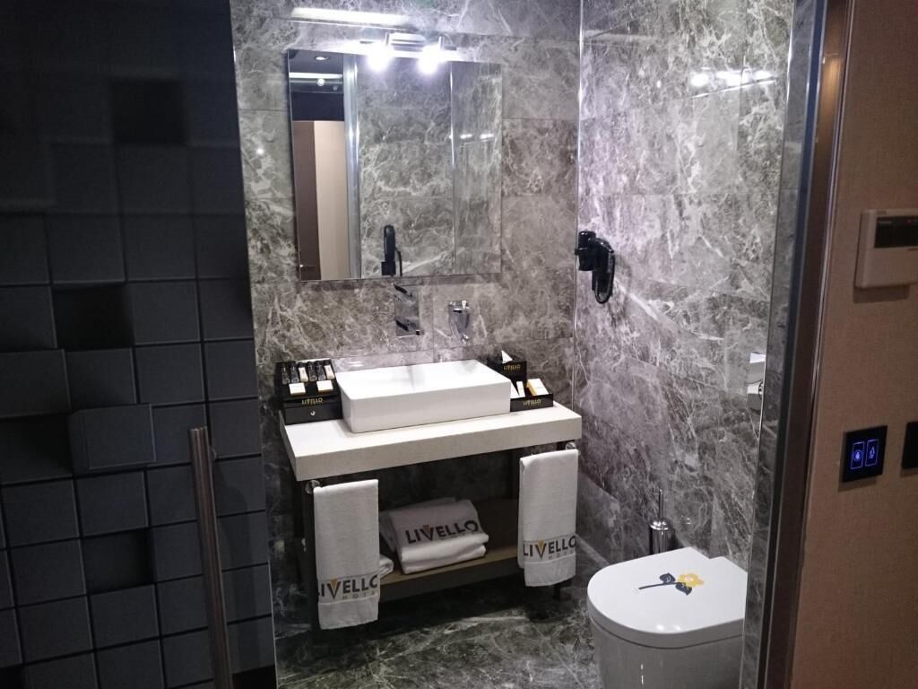 Une salle de bain moderne avec un meuble-lavabo en marbre, un miroir, des toilettes et deux serviettes étiquetées « LIVELLO ».