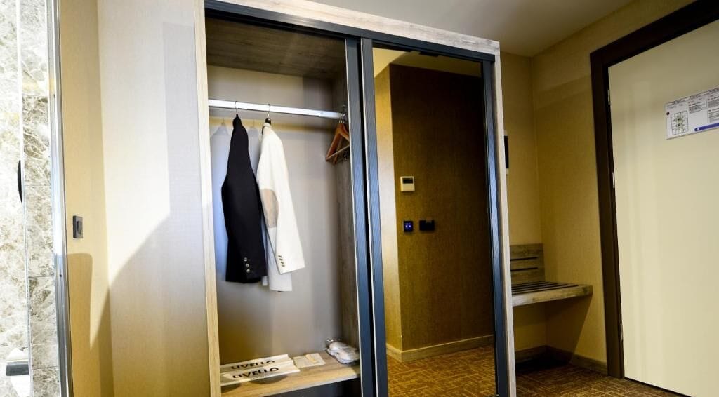Une chambre d’hôtel avec une porte de placard coulissante, une petite table avec un téléphone et un banc.