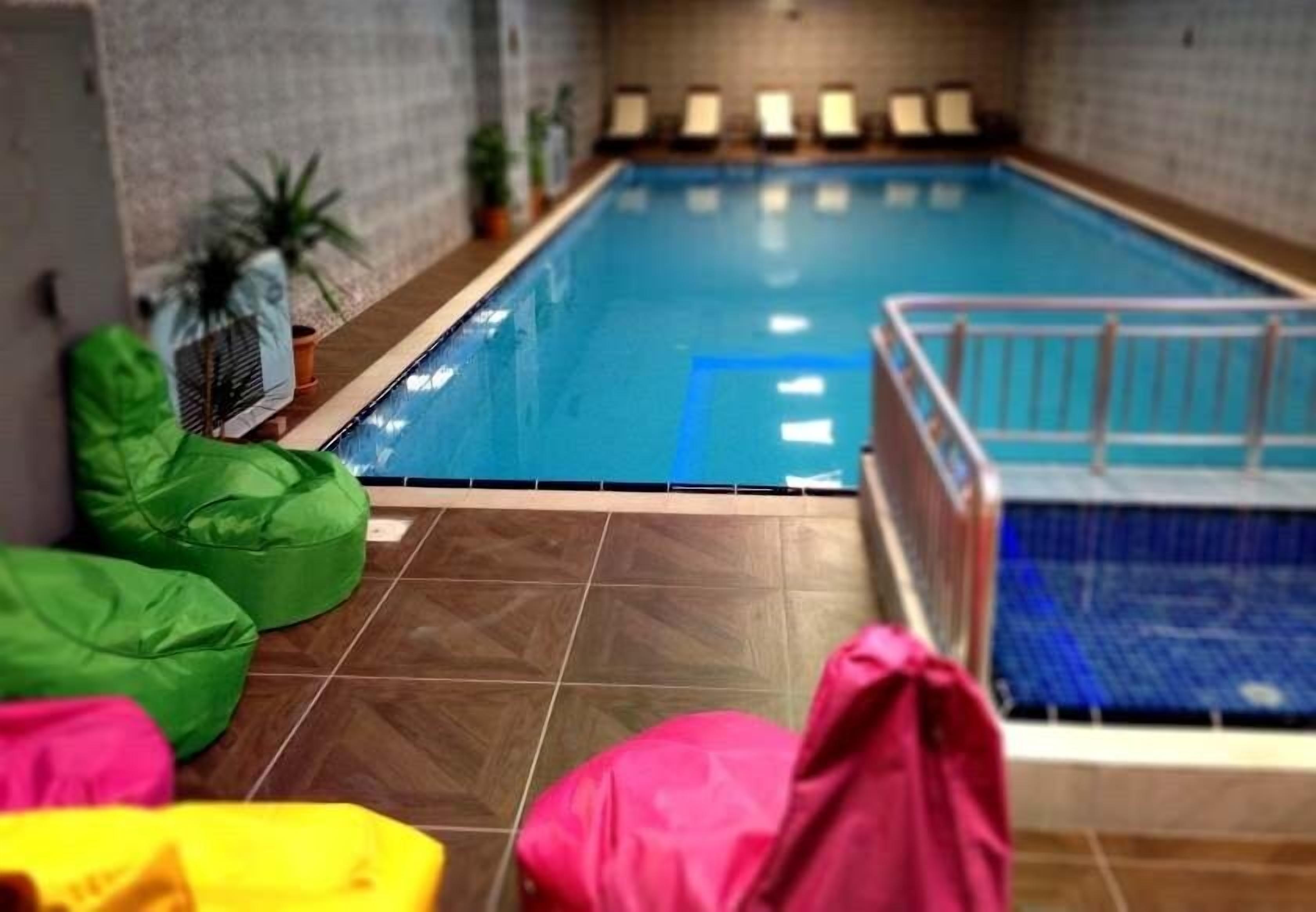 An indoor swimming pool with a tiled floor, a poolside area with seating, and a small pool lift.