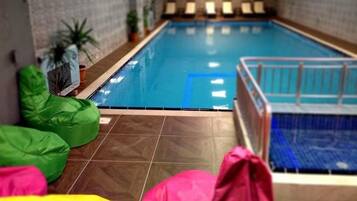 An indoor swimming pool with a tiled floor, a poolside area with seating, and a small pool lift.