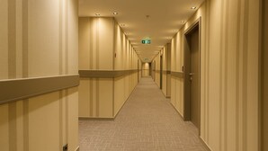 Ein langer, schmaler Hotelkorridor mit Teppichmuster, beigen Wänden und Türen an beiden Seiten.
