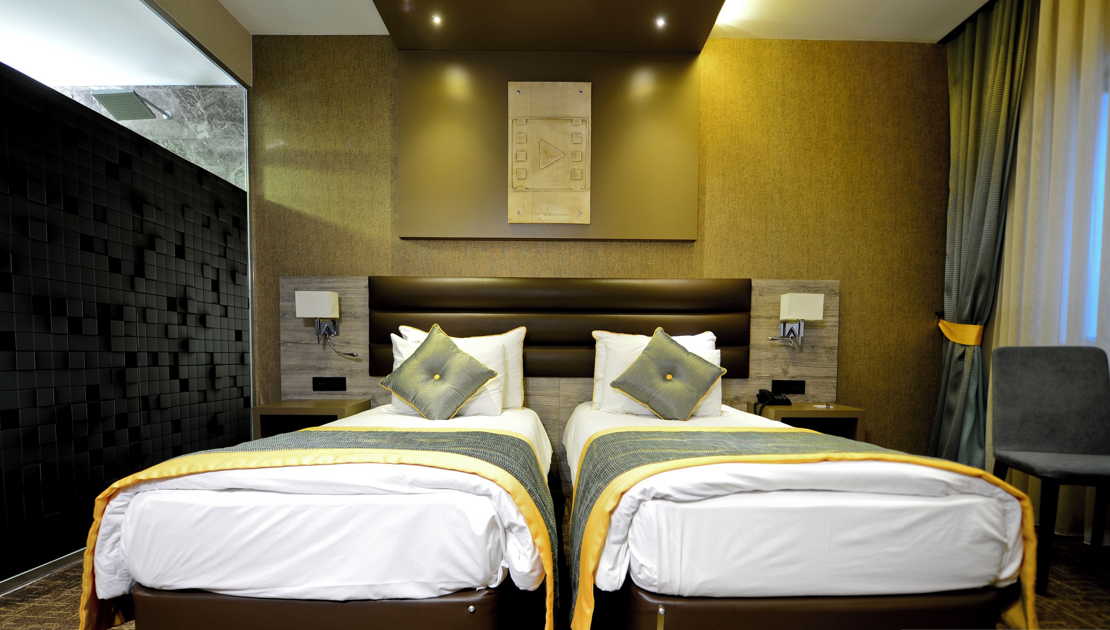 A hotel room with two beds, a large headboard, a wall-mounted artwork, and a view through a window.