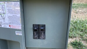 A utility box with two circuit breakers, a grounding rod, and a warning label.