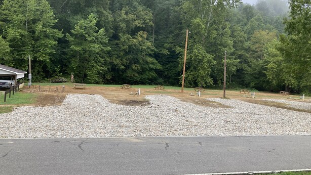 A gravel parking area with picnic tables and a building in the background.