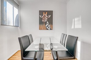 A modern dining room with a glass table and leather chairs, a giraffe painting on the wall, and a window with blinds. - Apartment 'Gandia Center' with Balcony, Wi-Fi and Air Conditioning (Gandía)