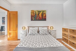 Ein Schlafzimmer mit einem Bett, zwei Nachttischen, einem Holzschrank, einem Bild an der Wand und einer Tür.