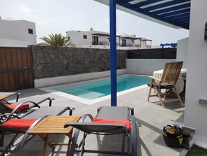 Un espace piscine comprenant des chaises longues, une table et un mur en pierre.