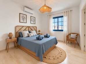 A bedroom with a bed, a bedside table, a chair, a window with curtains, and a hanging light fixture.