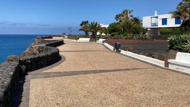 A coastal walkway with a stone wall, palm trees, and a white building with blue accents. - Villa Maria Luisa near the beach with private pool and Wi-Fi (Playa Blanca)