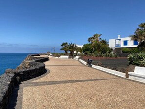 Une promenade en bord de mer, bordée d’un mur de pierres, de palmiers et d’un bâtiment blanc agrémenté de touches de bleu.