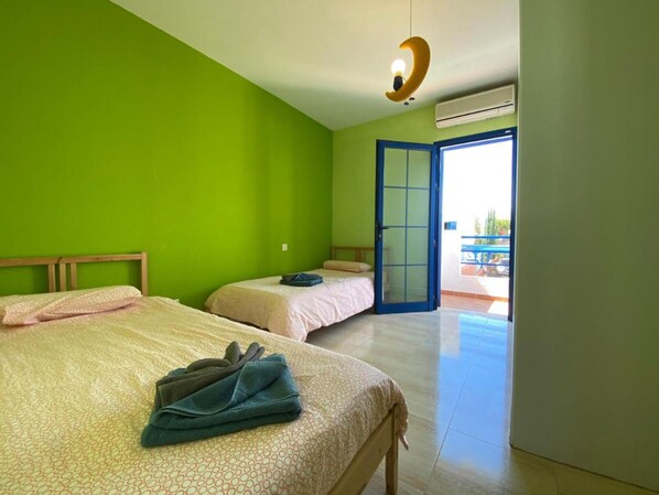 Une chambre avec deux lits, une porte bleue et un appareil de climatisation.