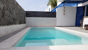 A rectangular swimming pool with tiled edges, a stone wall on one side, and a blue staircase leading to a white building with a blue door. - Villa Maria Luisa near the beach with private pool and Wi-Fi (Playa Blanca)