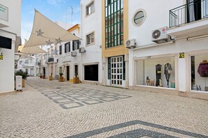 Eine Kopfsteinpflasterstraße mit Gebäuden, ein beschatteter Bereich mit Sterndekorationen und ein Geschäft mit Schaufensterfiguren.