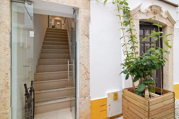 Eine Treppe, die zu einem Innenraum führt, ein hölzerner Pflanztopf mit einer Pflanze und eine Tür mit dekorativem Bogenbogen.