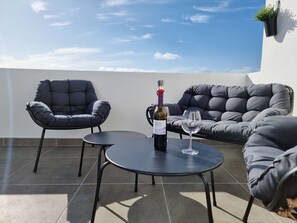 Una terraza en la azotea con dos sillas, una mesa y una botella de vino.