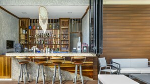 A bar area with wooden shelves, bar stools, and a white sofa. - Oceana Home Travel Mexico  (Playa del Carmen)