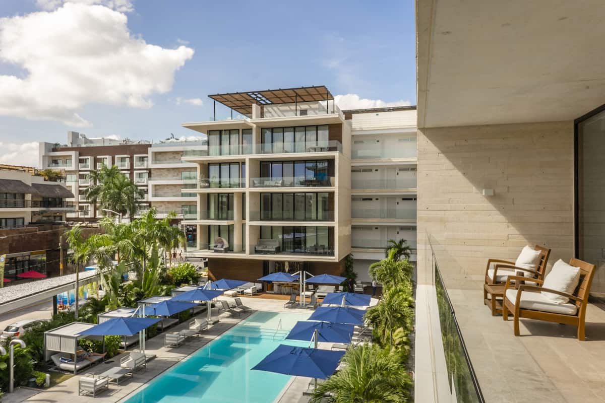 A modern hotel with a rooftop pool, multiple balconies, and outdoor seating areas.