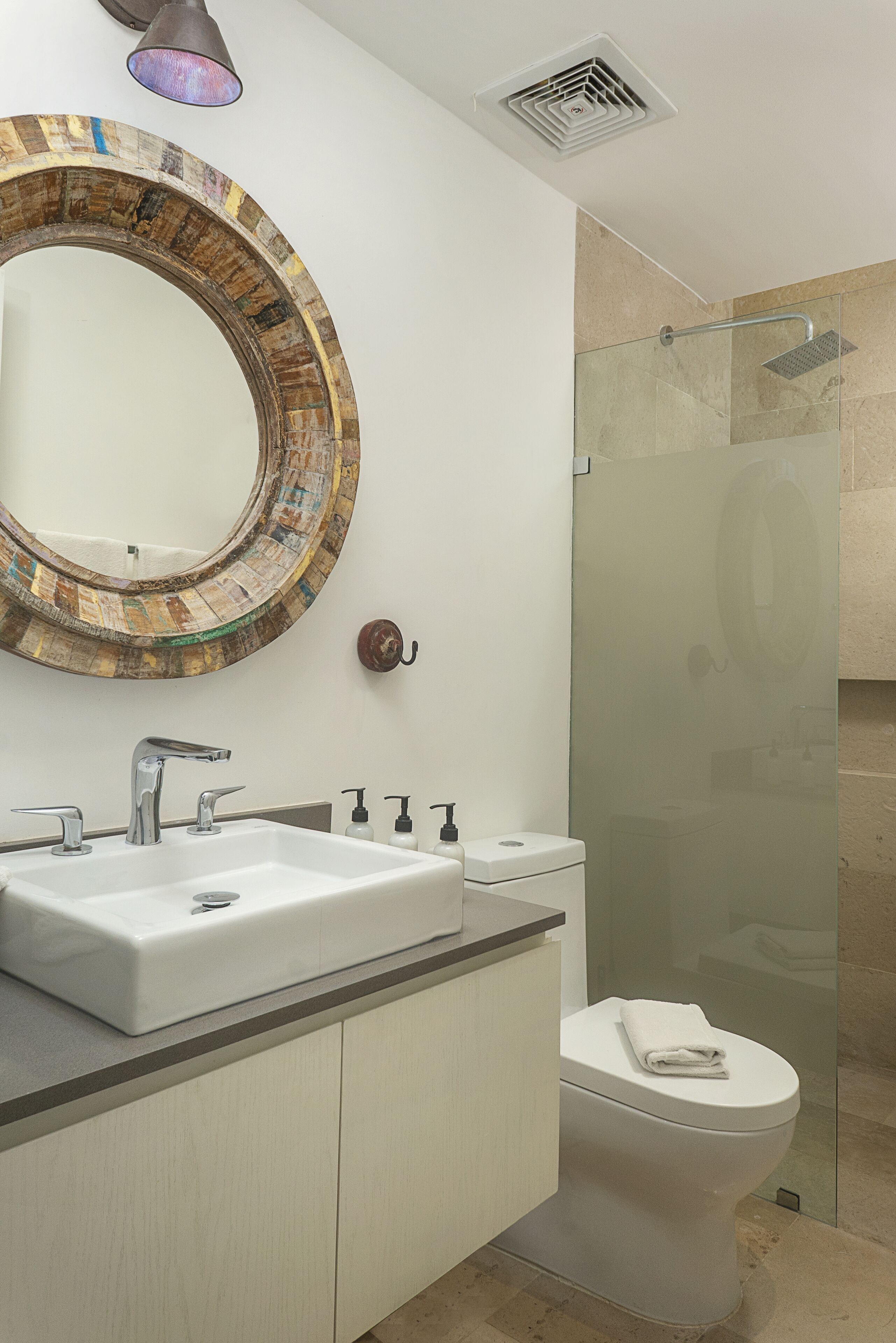 Une salle de bain moderne avec un miroir rond, un lavabo blanc, des toilettes et une douche à parois de verre.