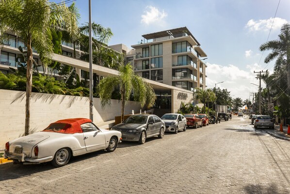 Una calle bordeada de vehículos estacionados y un edificio moderno con balcones.