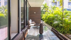 A modern outdoor seating area with glass tables and benches, surrounded by lush greenery and a view of a building with large windows. - Oceana Home Travel Mexico  (Playa del Carmen)