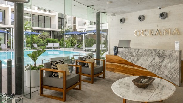 A modern hotel lobby with a pool view, seating area, and a reception desk. - Oceana Home Travel Mexico  (Playa del Carmen)