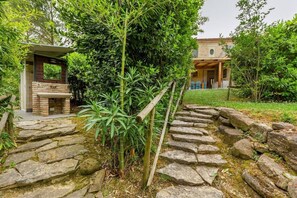 A stone pathway leading to a brick-built outdoor seating area, surrounded by lush greenery and a residential building in the background. - Villa "Casa della Musica" with Shared Pool, Garden & Wi-Fi (Ostra)