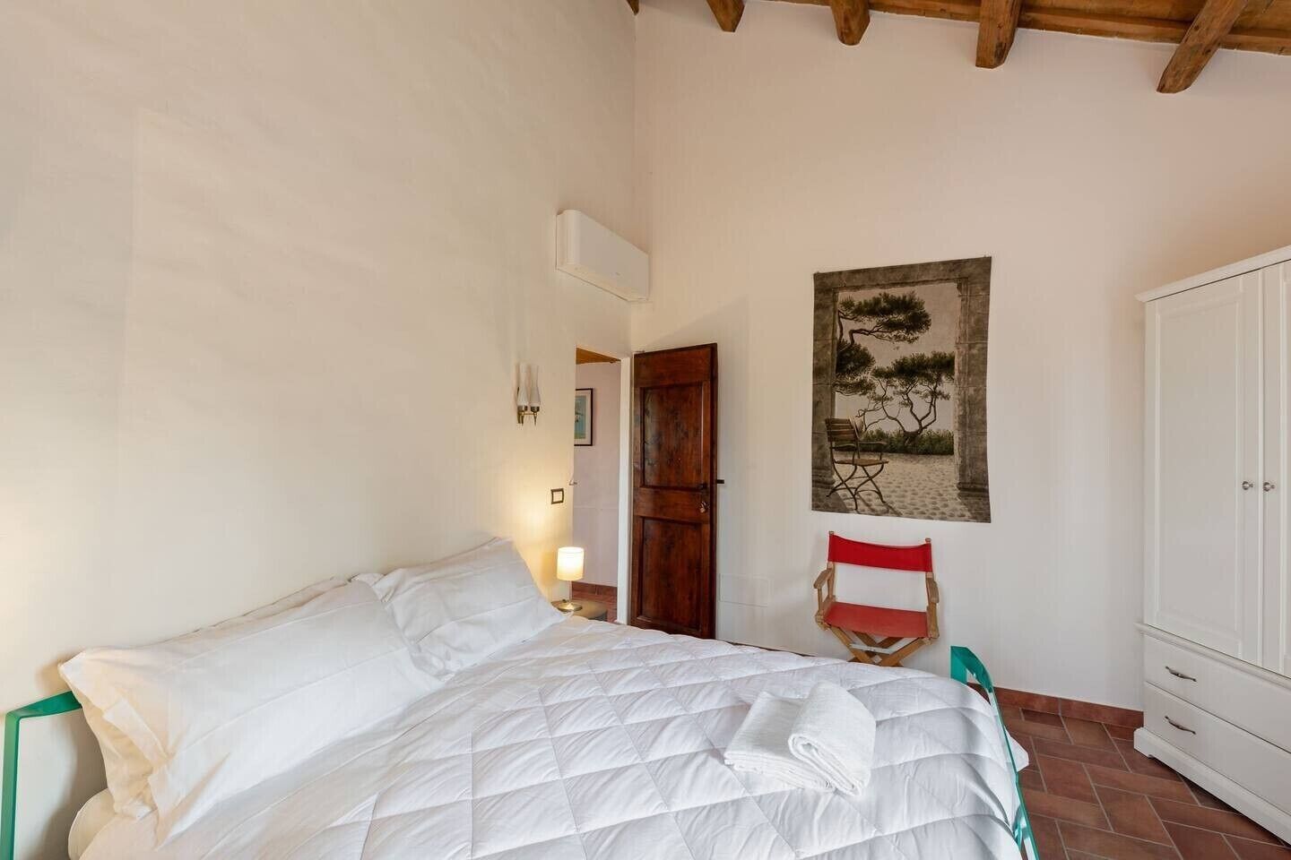 A bedroom with a bed, a chair, a wardrobe, and a painting on the wall.