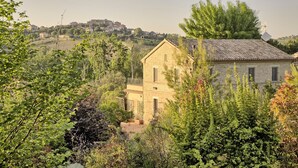 Un bâtiment en pierre doté d’un balcon, entouré de verdure et surplombant une ville lointaine.