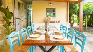 Une table à manger en bois, entourée de chaises bleues, un vase servant de centre de table et, au fond, une cuisine.