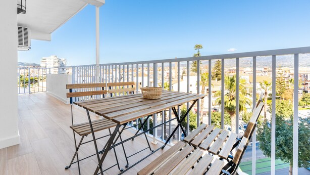 A balcony with a wooden table, chairs, and a basket.