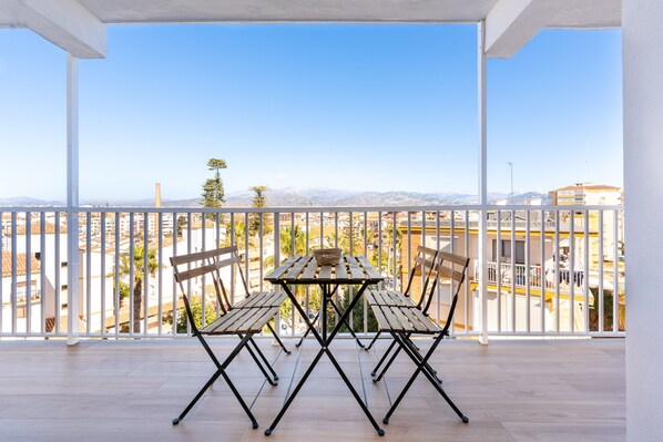 Un balcon avec une table et des chaises en bois, une balustrade blanche et une vue sur les bâtiments et les montagnes.