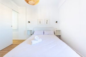 Un lit bien fait, avec une serviette roulée, des murs blancs, un luminaire suspendu et deux tables de chevet avec des lampes.