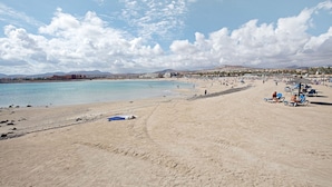 Ein Strand mit blauem Himmel, sandigem Ufer und einigen Personen.