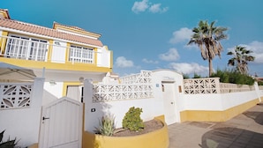 Ein Wohngebäude mit weißer und gelber Fassade, einem verschlossenen Eingang und einer kleinen Gartenanlage.