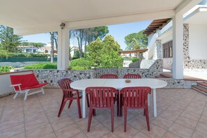 An outdoor patio with a white table and red chairs, a red sofa, and a stone wall.