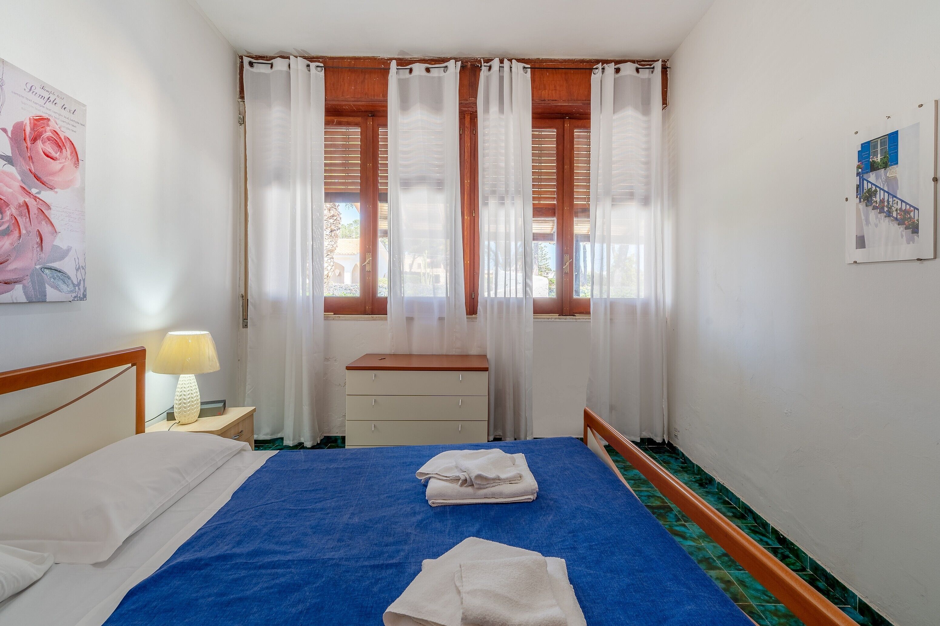 A bedroom with a bed, a nightstand, a dresser, and a window with curtains.