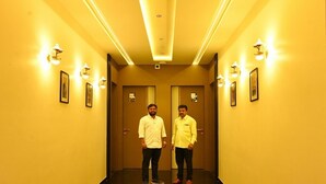 A hallway with two doors, each marked with a number. The walls are yellow, and there are wall-mounted lights along the corridor. - The Dorm Inn (Nashik)