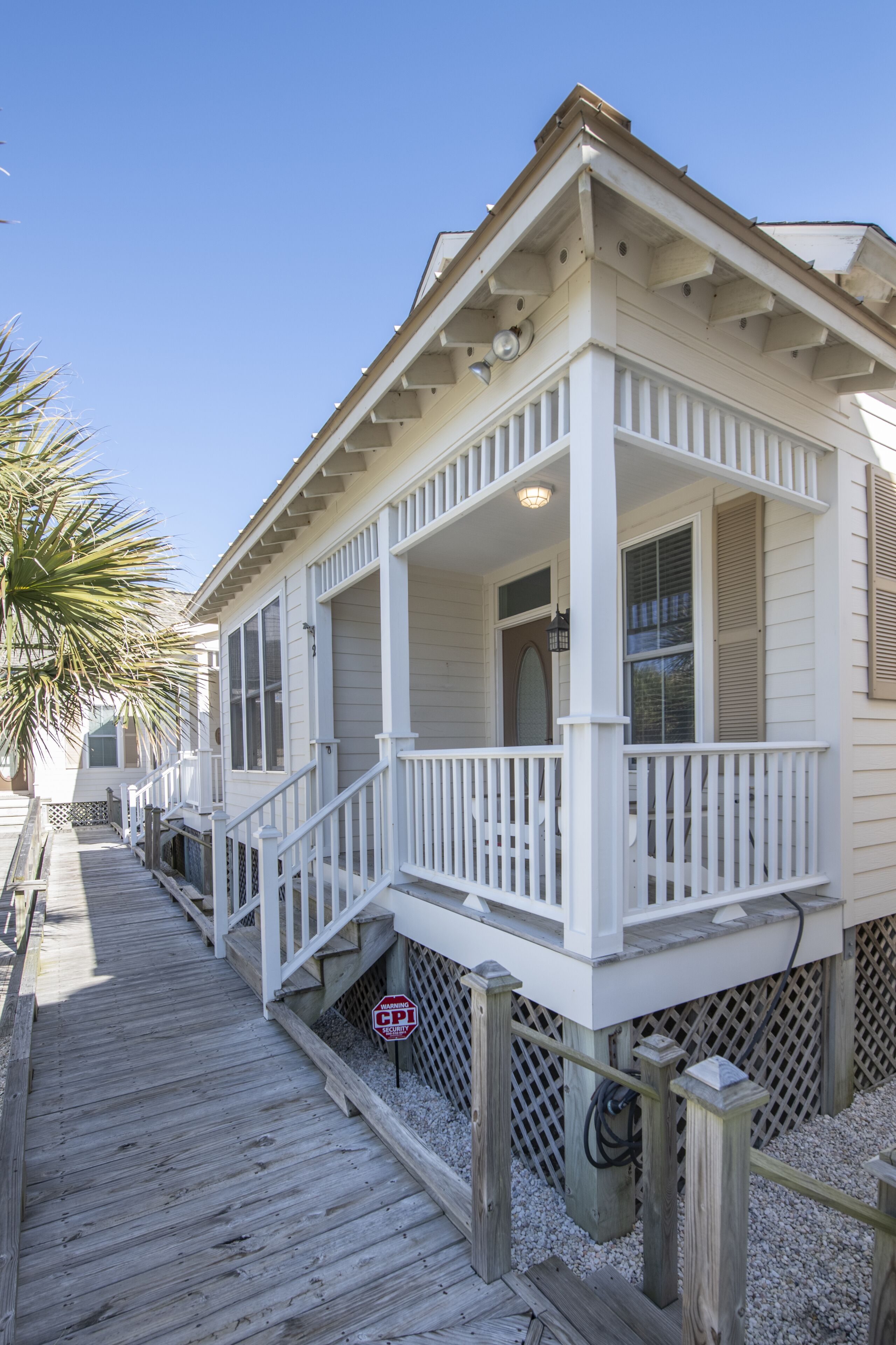 A white wooden house with a porch, a wooden deck, and a palm tree.