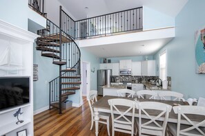 Enjoy meals in the central dining area with a wooden table and white chairs, surrounded by a spiral staircase and balcony.