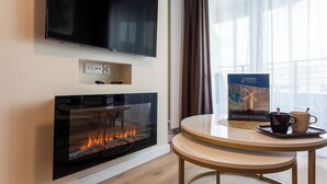 Ett modernt rum med en öppen spis, en platt-TV som är monterad på väggen, ett bord med ett bricka och koppar samt ett fönster med gardiner.