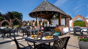Eine Terrasse im Freien mit Ziegelbögen, einer Laube und Tischen mit Stühlen.